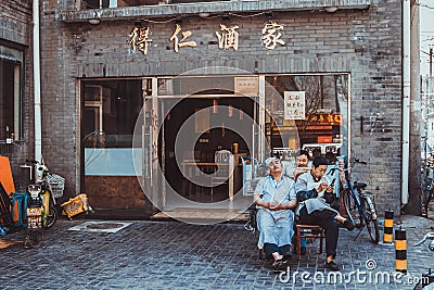 Three chinese restaurant workers sitting on chairs on street of Beijing in front of a restaurant Editorial Stock Photo