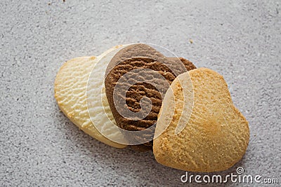 Three close-up sweet heart-shaped cookies: vanilla, lemon, chocolate on the left. Gray background Stock Photo