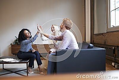 Three colleagues high five at a casual work meeting Stock Photo