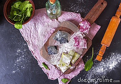 Three color homemade raw pink beetroot, green spinach and black cuttlefish ink pasta ravioli with cheese and parsley on a brown Stock Photo