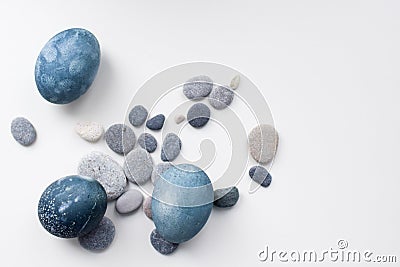 Three colored blue, gray marble eggs lie on a white background among the stones Stock Photo