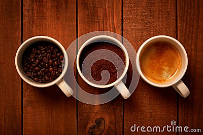 Three cups of espresso, freshly ground coffee and coffee beans on a wooden table Stock Photo