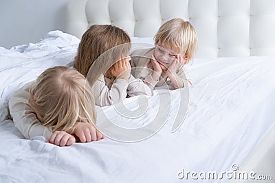 three cute kids girl and boys brothers and sister smiling lying on bed at light modern bedroom Stock Photo