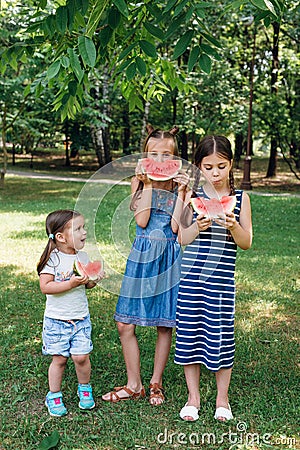 Three cute little sisters eating watermelon in park in summertime Stock Photo