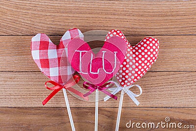 Three different fabric hearts on wooden sticks with ribbon bows placed on a wooden background. Photo Valentines Day Stock Photo