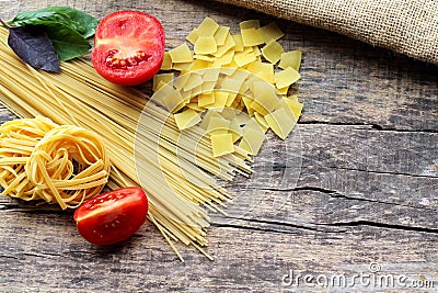 Three different types of pasta with fresh purple and green basil and red tomatoes on a wooden background with a place for text Stock Photo