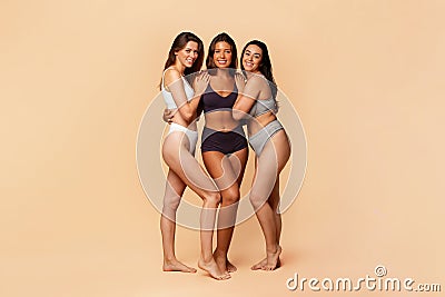 Three diverse millennial women in casual undergarments stand close, embracing each other Stock Photo
