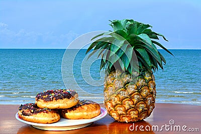 Three donuts placed on a plate and pineapple placed on a wooden Stock Photo