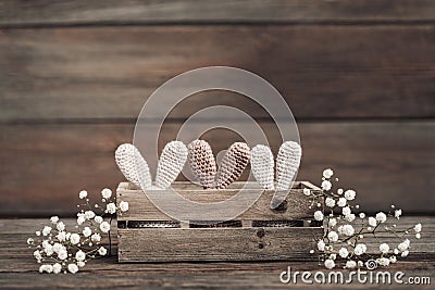 Three Easter eggs in crocheted hats with rabbit ears in a wooden box on a rustic wooden table. Stock Photo