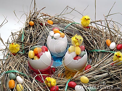 Three egg shells in a cup filled with colorful coated eggs Stock Photo