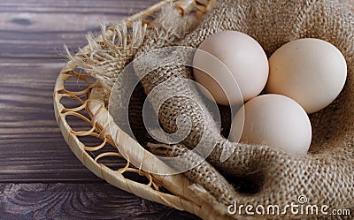 Three eggs lie on a sackcloth in a wicker basket. Stock Photo