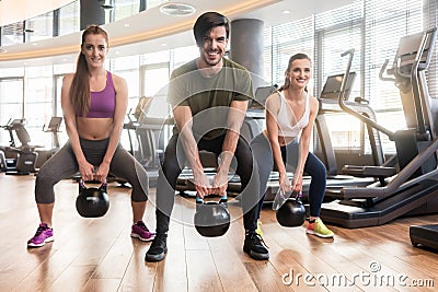 Three fit young people exercising kettlebell swings during full- Stock Photo