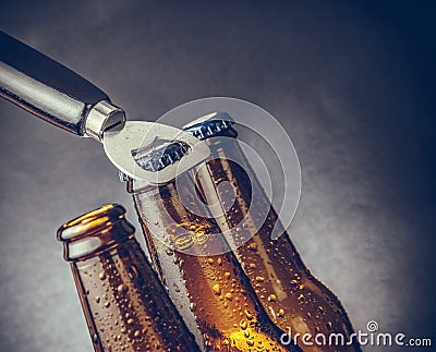 Three fresh cold beer ale bottles with drops and stopper open with bottle opener Stock Photo