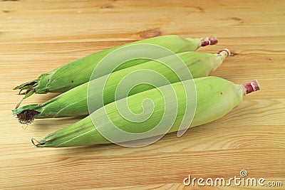 Three fresh purple corns with bright green husks and silks isolated on wooden background Stock Photo