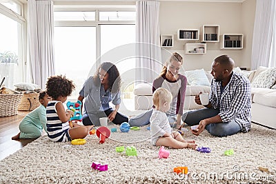 Three friends playing with toddlers on sitting room floor Stock Photo