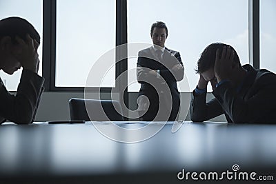 Three frustrated and overworked business people in the board room with arms crossed and head in hands. Stock Photo