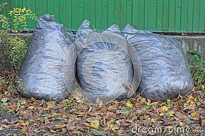 three full gray plastic bags with garbage stand on the ground near the wall Stock Photo