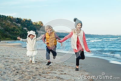 Three funny smiling laughing white Caucasian children kids friends playing running on ocean sea beach on sunset outdoors Stock Photo