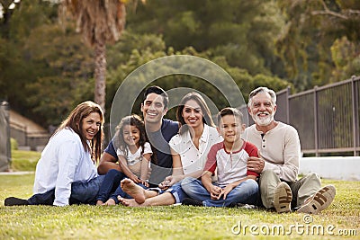 Three generation Hispanic family sitting on the grass in the park smiling to camera, selective focus Stock Photo