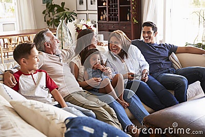 Three generation Hispanic family sitting on the sofa watching TV, grandmother using remote control Stock Photo