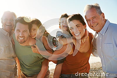 Three generation white family on a beach smiling to camera, parents piggybacking kids, close up Stock Photo