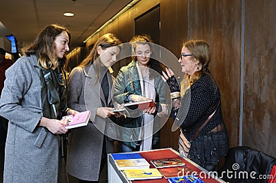 Three girls with books in hands standing in front of bookseller telling customers about books available Editorial Stock Photo