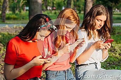 Three girls chatting with their smartphones at the park. Gen Z young girl friends using gadget and having fun outdoors Stock Photo