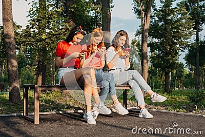 Three girls chatting with their smartphones at the park. Gen Z young girl friends using gadget and having fun outdoors Stock Photo