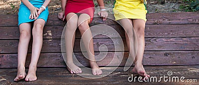 Three girls are sitting side by side on a bench. Slender tanned legs of girlfriends. Healthy bare feet. No flat feet Stock Photo