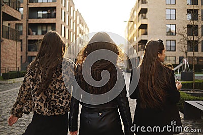 Three girls walk in the summer, girls go for a walk, evening at sunset. Smartly dressed girls, friendship, fashion. Brunettes walk Stock Photo