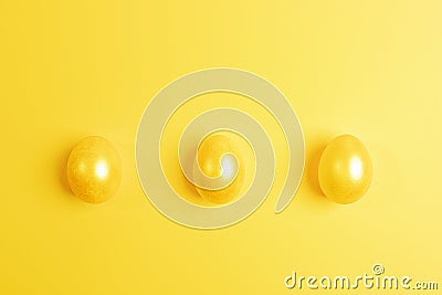 Three glossy painted yellow Easter eggs are lying in row on yellow background. Top view Stock Photo