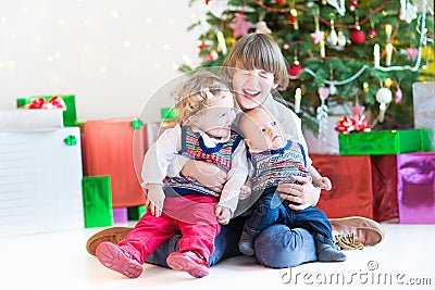 Three happy children - teenager boy, toddler girl and their newborn baby brother - playing together under Christmas tree Stock Photo