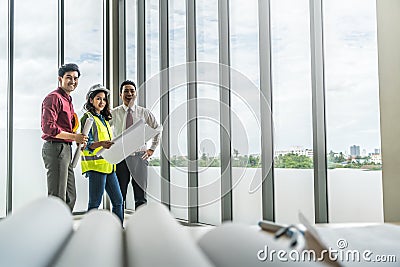 Three happy contractor team smiling at the far end of a desk full of building plans Stock Photo