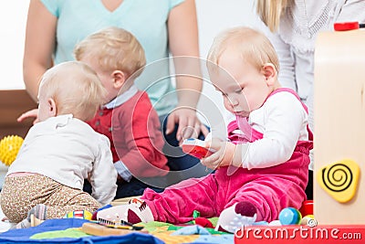 Three happy mothers watching their babies playing with safe multicolored toys Stock Photo