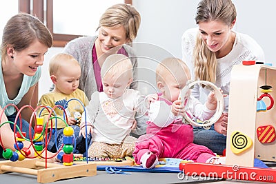 Three happy mothers watching their babies playing with safe multicolored toys Stock Photo