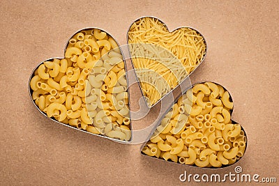 Three hearts of pasta on brown paper background. Art design. Vintage parchment. Shape of heart, symbol of love. Heap of uncooked m Stock Photo