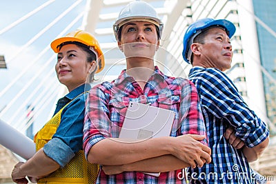 Three Industrial engineer wear safety helmet engineering standing with arms crossed on building outside. Stock Photo