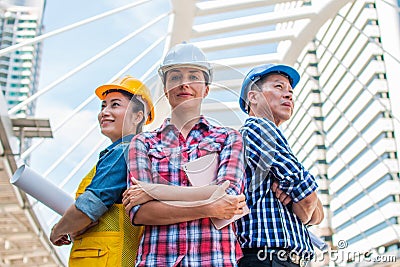 Three Industrial engineer wear safety helmet engineering standing with arms crossed on building outside. Stock Photo