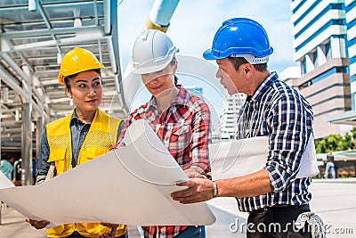 Three industrial engineer wear safety helmet engineering working and talking with drawings inspection on building outside Stock Photo