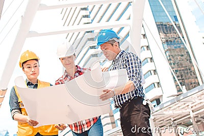 Three Industrial engineer wear safety helmet engineering working and talking with drawings inspection Stock Photo