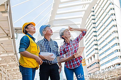 Three industrial engineer wear safety helmet and holding tablet engineering working and talking with drawings inspection Stock Photo