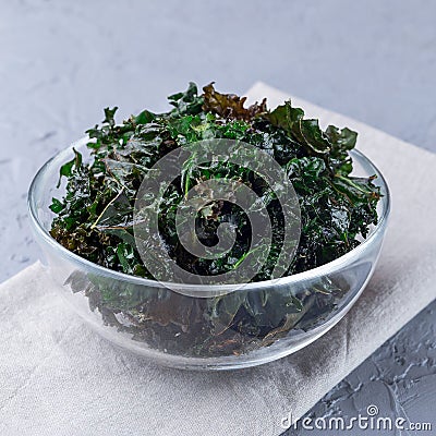 Three ingredient baked green kale chips with sea salt and olive oil, in glass bowl, square format Stock Photo