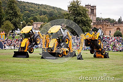 Three JCB Backhoe loaders with vehicle passing underneath them, dancing diggers Editorial Stock Photo