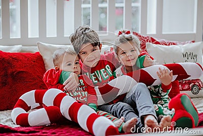 Three kids in Christmas pyjamas laying on white big bed with Christmas pillows Stock Photo