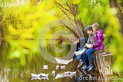 Three kids near the pond putting paper boats Stock Photo