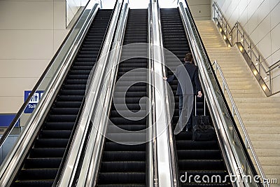 Three large escalators with a man in a business suit carrying a suitcase riding up on one of them Stock Photo