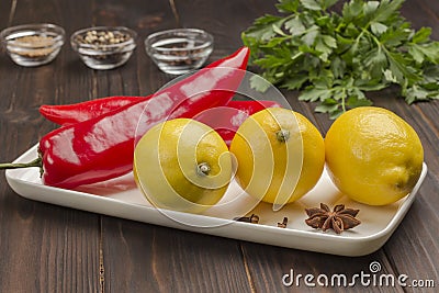 Three lemons and two chili peppers on white plate, parsley and spices Stock Photo