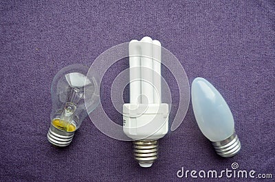 Three light bulbs. A white energy-saving fluorescent bulb with four tubes, an oblong incandescent bulb with gray glass, a round or Stock Photo