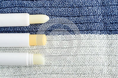 Three lip balms on the knitted background. Winter lip care sticks with beeswax, honey, panthenol and shea butter. Copy space. Stock Photo