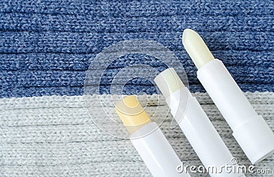 Three lip balms on the knitted background. Winter lip care sticks with beeswax, honey, panthenol and shea butter. Stock Photo